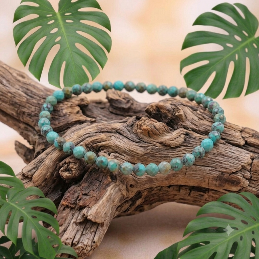 Un bracelet de perles rondes facettées en turquoise est posé sur un morceau de bois flotté texturé et vieilli. L'arrière-plan est décoré de grandes feuilles de Monstera vert vif. La perspective est un plan moyen légèrement en plongée avec un éclairage naturel doux.