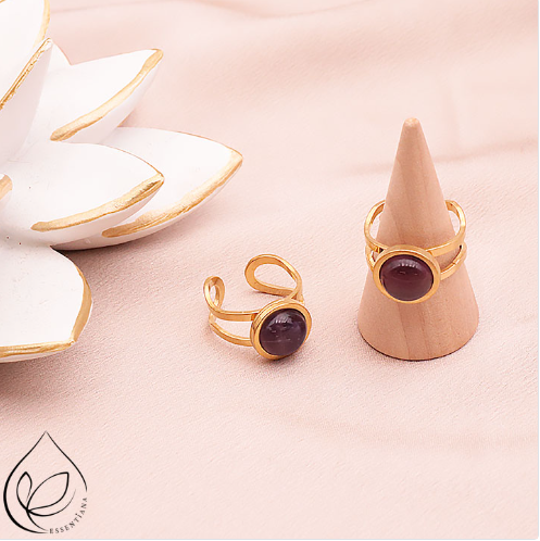 Deux bagues en améthyste style Azélis doré sur un fond clair et lumineux : une bague posée à plat et l’autre sur un petit présentoir en forme de cône, pierre centrale de 10 mm, monture en acier inoxydable professionnel, bagues artisanales, couleurs violet et doré, bijou élégant et durable, idéal pour style et bien-être.