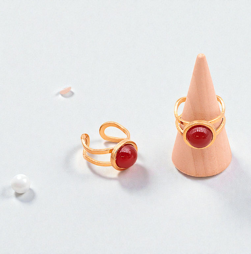 Deux bagues en cornaline style Azélis doré sur un fond clair et lumineux : une bague posée à plat et l’autre sur un petit présentoir en forme de cône, pierre centrale de 10 mm, monture en acier inoxydable 304 professionnel, bagues artisanales, couleurs orange et doré, bijou élégant et durable, idéal pour style et bien-être.