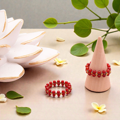 Deux bagues en cornaline rouge avec perles dorées sur un fond clair : une posée à plat et l’autre sur un petit présentoir en forme de cône, perles naturelles doublées de 3 mm, bagues artisanales, bijou éclatant et raffiné.