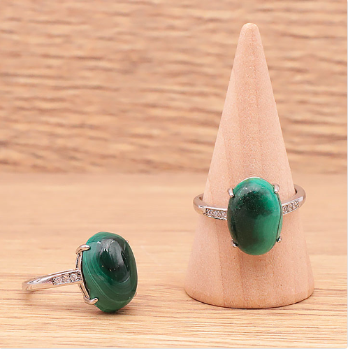 Deux bagues en malachite naturelle du Congo sur un fond clair et lumineux : une posée à plat et l’autre sur un petit présentoir en forme de cône, pierre ovale verte de 14 x 0,7 mm, monture en laiton argenté réglable, bijou artisanal et élégant.