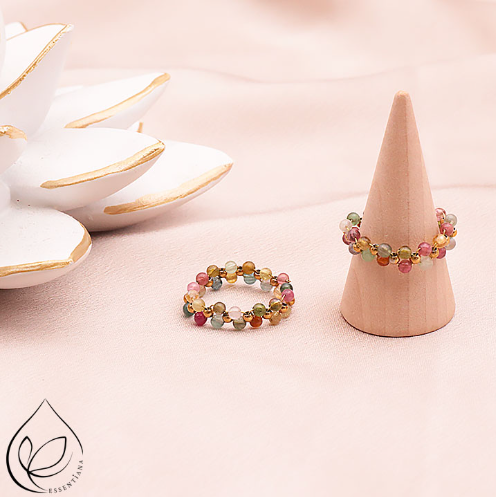 Deux bagues en tourmaline multicolore présentées sur un fond clair et lumineux : une bague posée à plat et l’autre sur un petit présentoir en forme de cône, pierres naturelles de qualité AA+, perles de 3 mm, bijou artisanal fait main, éclat et couleurs bleu, doré, jaune, rose et vert.