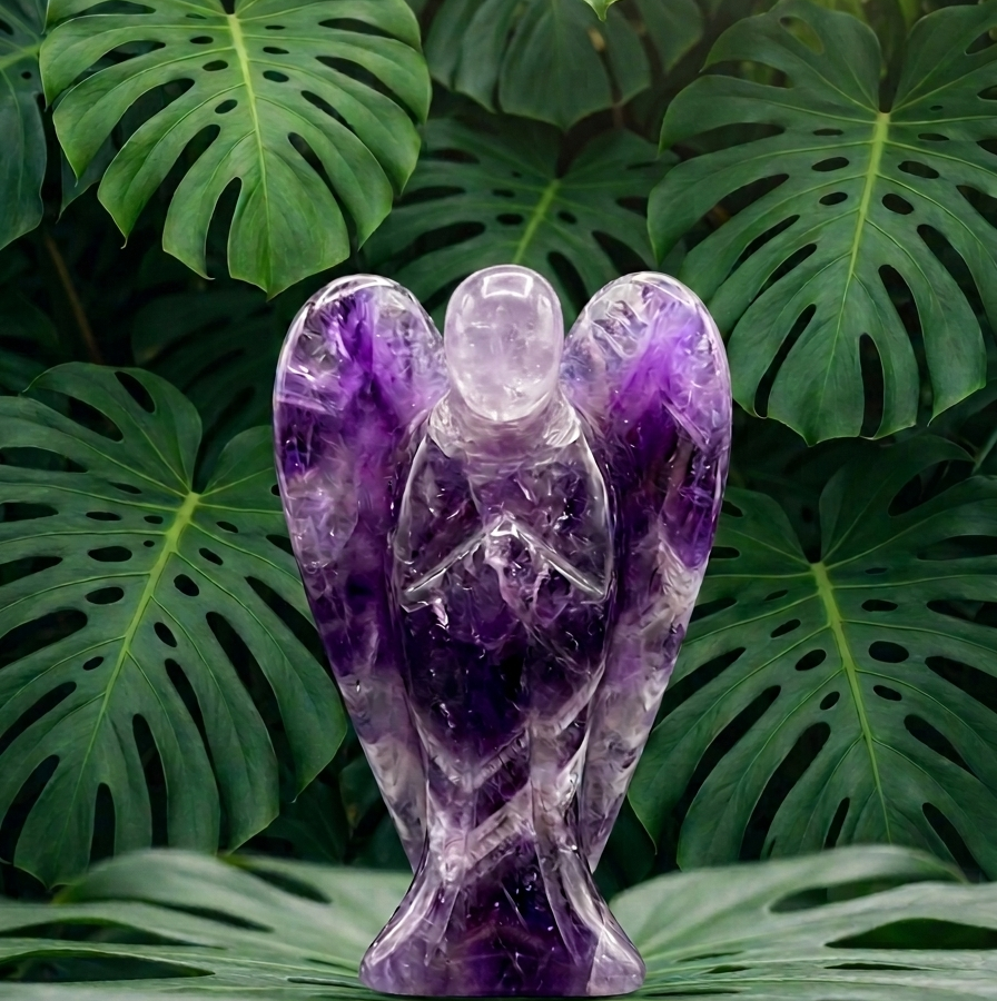 Une statuette d'ange sculptée en améthyste violette, aux ailes déployées et aux mains jointes, est posée au centre. Le visage est lisse et translucide, débarrassé de toute imperfection. L'objet repose sur une grande feuille de monstera d'un vert profond, devant un mur de feuillage exotique dense. La lumière douce met en valeur les reflets naturels et les nuances cristallines de la pierre violette.
