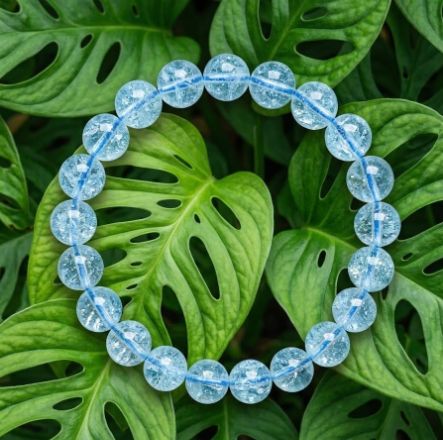 Ce bracelet se compose d'une série de perles rondes et lisses en topaze bleue translucide. Chaque perle est un motif régulier et captivant. L'ensemble est présenté sur un fond de feuilles de Monstera vertes naturelles font ressortir la clarté et la couleur unique du bijou.