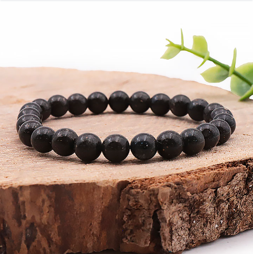 Ce bracelet circulaire est composé de perles rondes et lisses d'un noir profond, parsemées de minuscules inclusions pailletées multicolores évoquant une poussière d'étoiles.