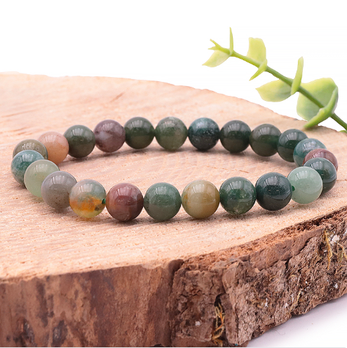 Un bracelet en agate indienne aux perles rondes et lisses de 8 mm, affichant une palette naturelle de verts moussus, de bruns terreux et de gris doux. Il repose élégamment sur une tranche de bois brut, devant une petite branche feuillue, évoquant une atmosphère de sérénité et de nature.