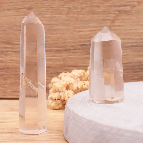 Deux pointes polies en cristal de roche fumé sont posées sur une table en bois clair. La plus grande à gauche est haute et svelte, tandis que la plus petite à droite est plus trapue. Les cristaux sont d'un brun fumé translucide, laissant entrevoir des inclusions intérieures naturelles et des reflets lumineux.