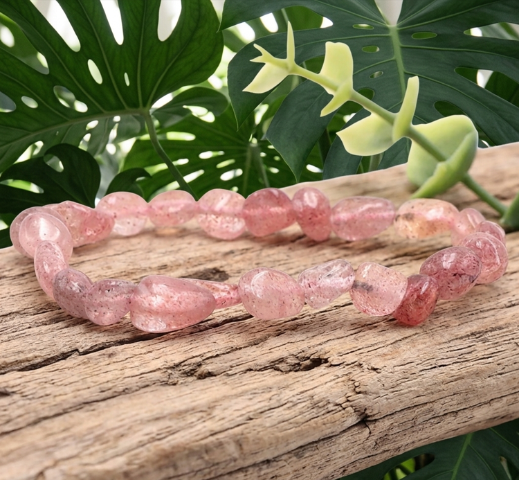 Un bracelet circulaire, formé de perles de quartz fraise roses et tachetées, est le point central de l'image. Il est délicatement posé sur une branche de bois flotté texturé, au cœur d'une forêt dense et profonde de feuilles de Monstera vert foncé. Le bois flotté et les feuilles de Monstera se complètent, créant une composition naturelle et multi-texturée, avec une petite pousse d'eucalyptus en haut à droite.