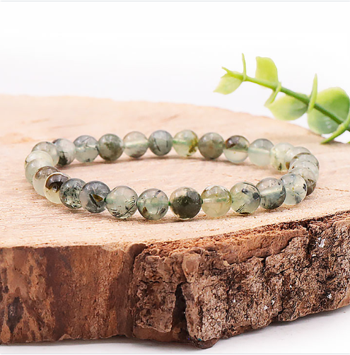 Un bracelet composé de perles de préhnite vert pâle, de forme régulière et semi translucide, est posé sur un morceau de bois