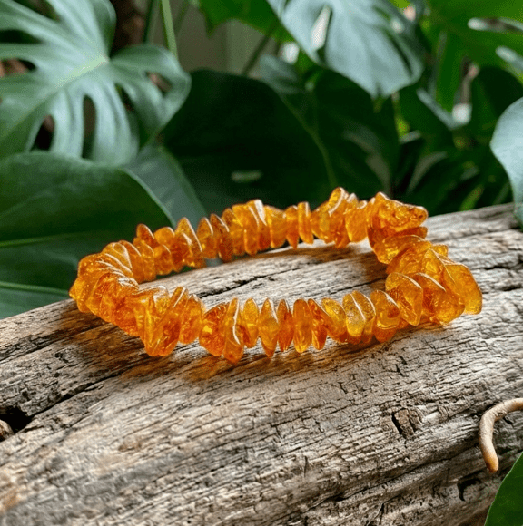 Un bracelet circulaire composé d'ambre brut, d'une couleur allant du jaune doré transparent à un orange ambré profond. Les perles sont des petits morceaux de formes et de tailles irrégulières, ce qui confère au bracelet un aspect naturel et organique. Elles sont enfilées sur un élastique transparent qui n'est pas visible.
